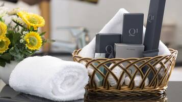A wicker basket containing toiletries, a rolled white towel, and a bouquet of yellow flowers.