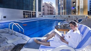 A poolside area with lounge chairs, a pool, and modern buildings in the background. - Baisan International Hotel Bahrain (Manama)