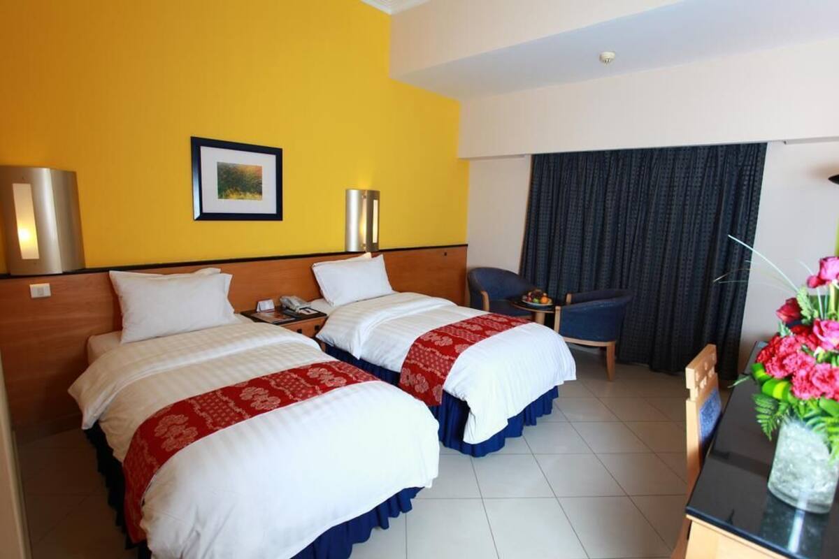 A hotel room with two beds, a desk, a chair, a small table, and a curtain.