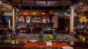 A restaurant with a bar area, wooden chairs, a table set for two with a vase of flowers, and a decorative ceiling. - Baisan International Hotel Bahrain (Manama)