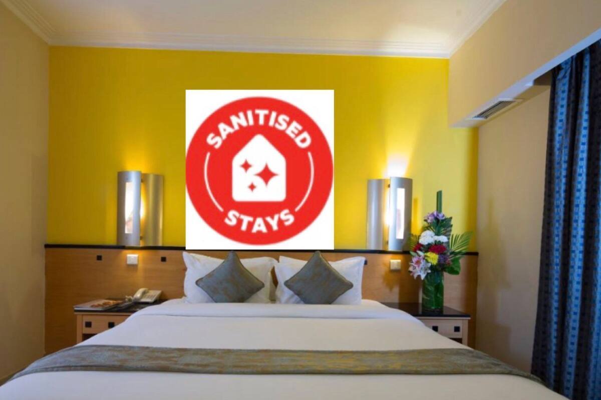 A hotel room with a bed, bedside lamps, a phone, and a sign indicating 'SANITISED STAYS'.