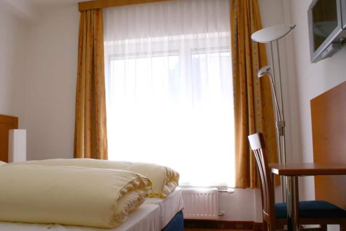 A hotel room with a bed, a window with curtains, a desk, and a lamp.