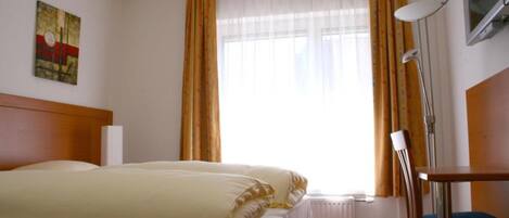 Ein Hotelzimmer mit Bett, einem Fenster mit Vorhängen, einem Schreibtisch und einer Lampe.