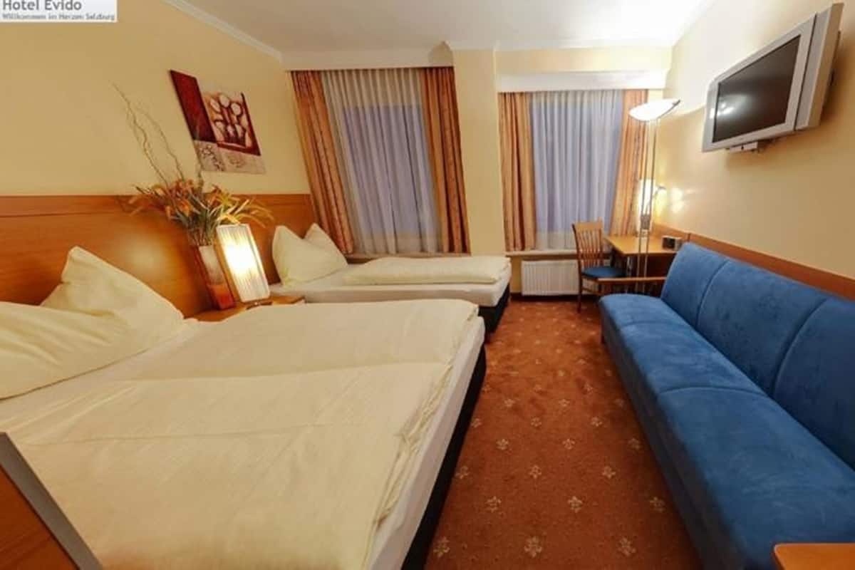 A hotel room with two beds, a blue sofa, a TV, and a small table.