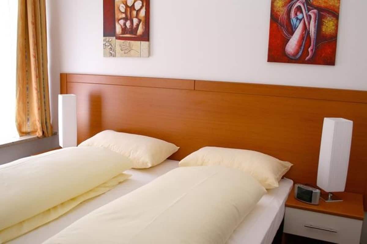 A double bed with white linens, a wooden headboard, two bedside tables with lamps, and artwork on the walls.