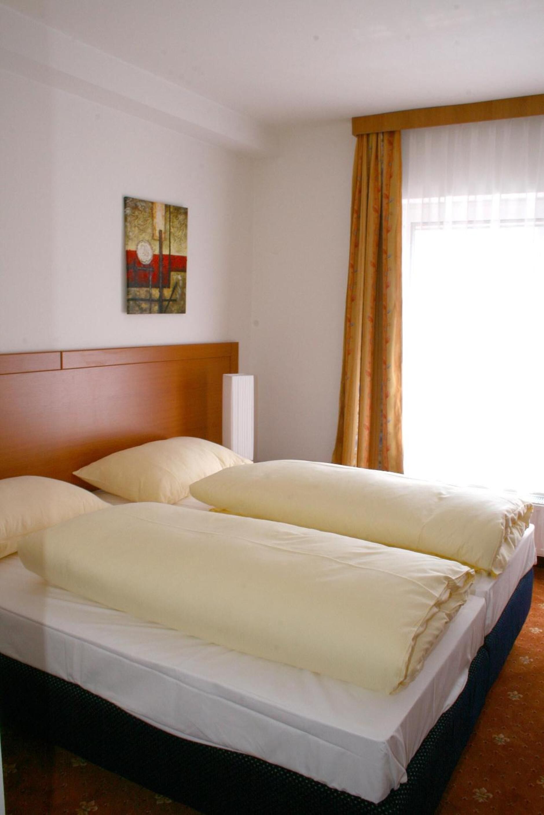 Habitación de hotel con cama doble, cabecera de madera, una obra de arte en la pared y ventana con cortinas.
