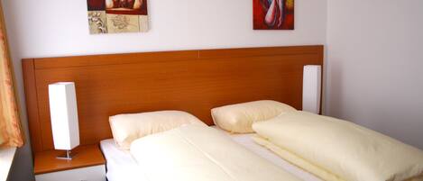 A hotel room with a wooden headboard, two beds with white bedding, a bedside table with a lamp, and two pieces of wall art.