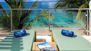 A balcony with two green cushioned chairs, a wooden table, and a book titled "SAINT MARTIN SIEHAARTEN". - Bleu Emeraude Hotel (Grand Case)