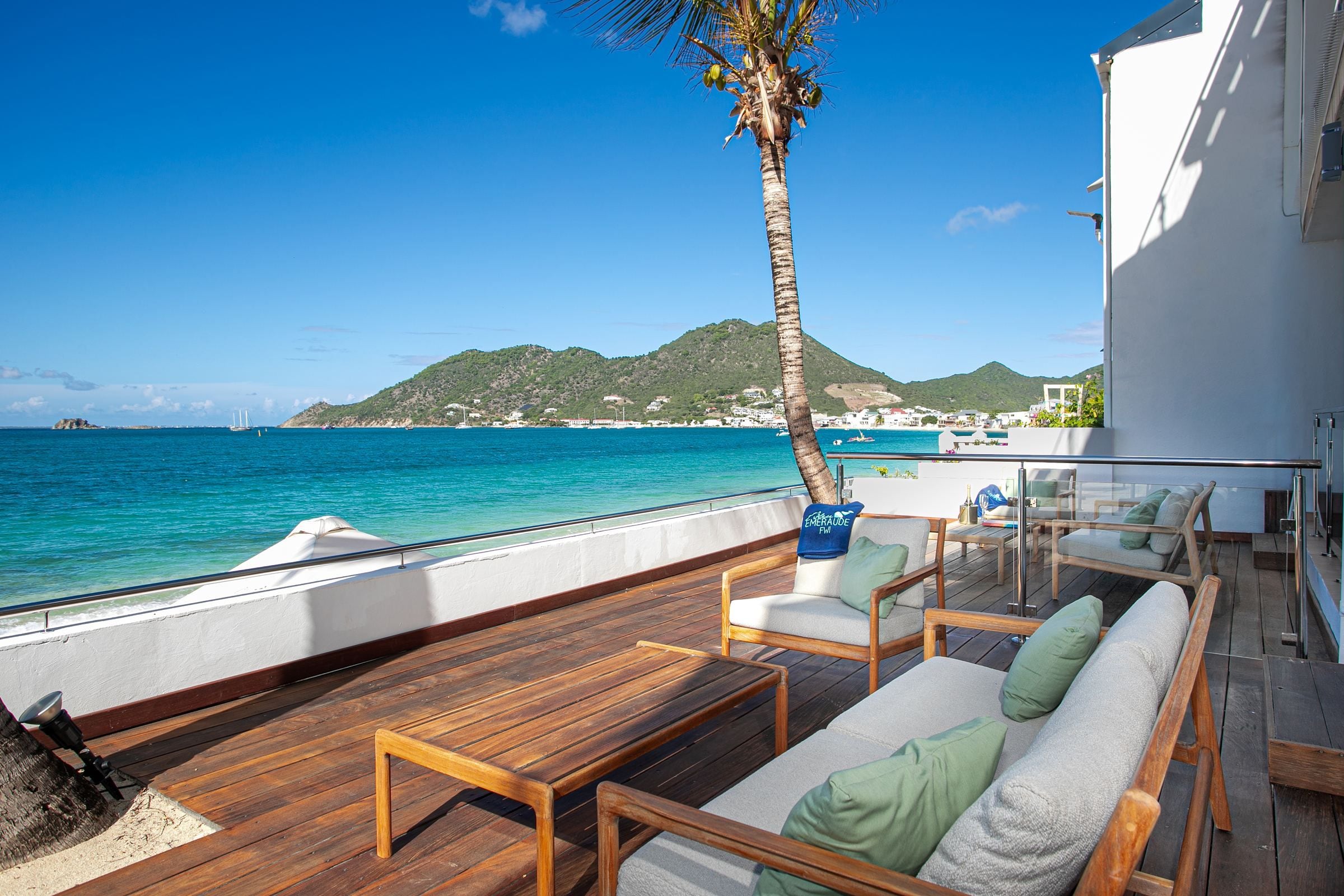 A deck with wooden furniture and a view of the sea and a mountain.