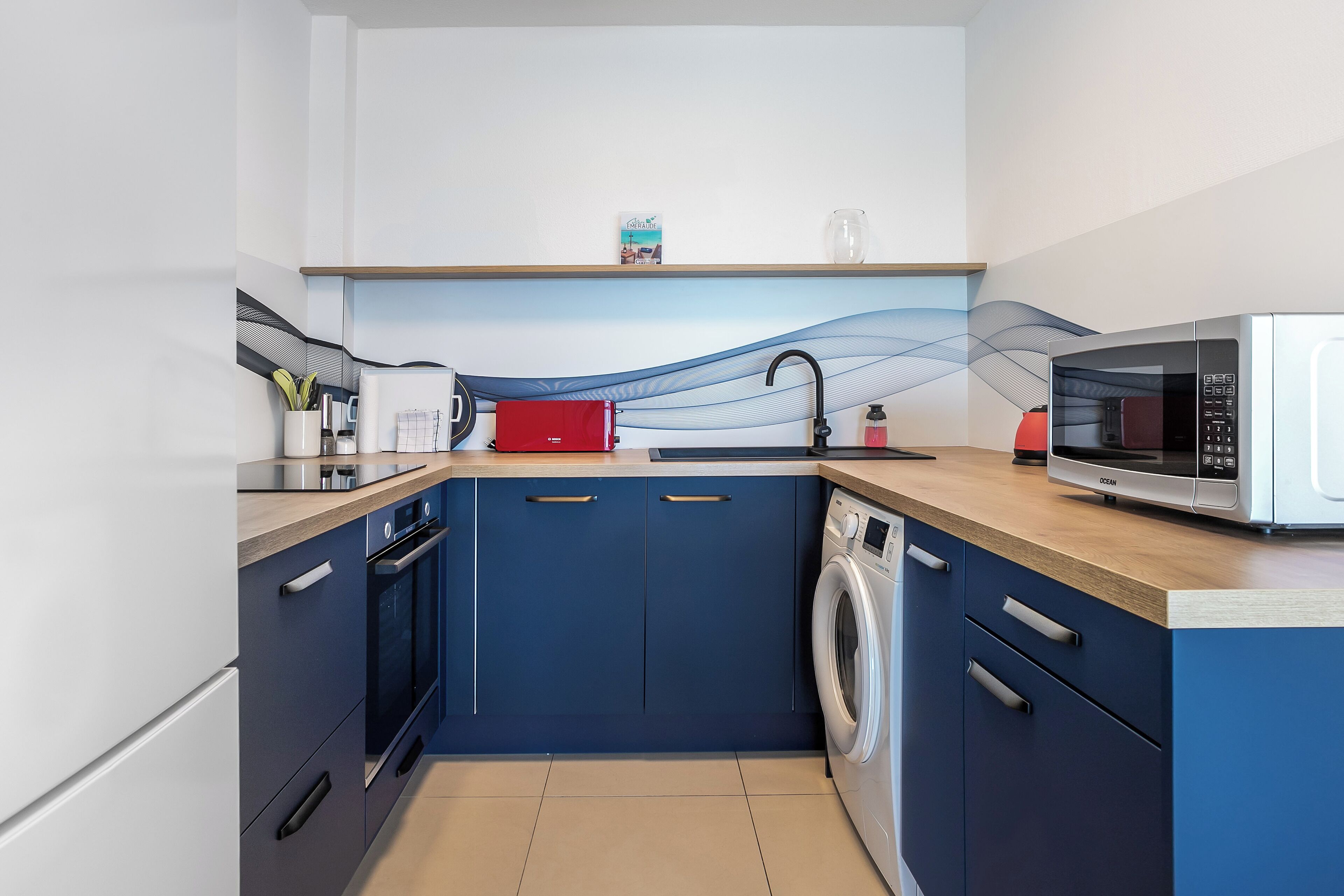 A compact kitchen with a microwave, a red kettle, and a washing machine.