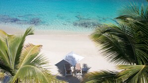 A beach with a white umbrella and two lounge chairs, palm trees, and clear turquoise water. - Bleu Emeraude Hotel (Grand Case)