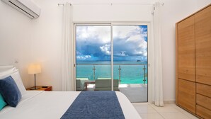 A hotel room with a bed, a nightstand, a lamp, a wooden wardrobe, and a balcony with a view of the sea. - Bleu Emeraude Hotel (Grand Case)