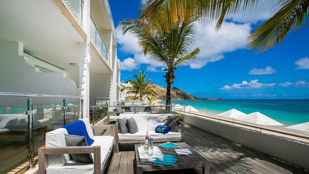 A deck with outdoor seating, a view of the ocean, and a palm tree. - Bleu Emeraude Hotel (Grand Case)