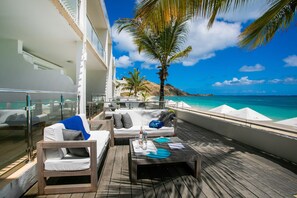 A deck with outdoor seating, a view of the ocean, and a palm tree. - Bleu Emeraude Hotel (Grand Case)