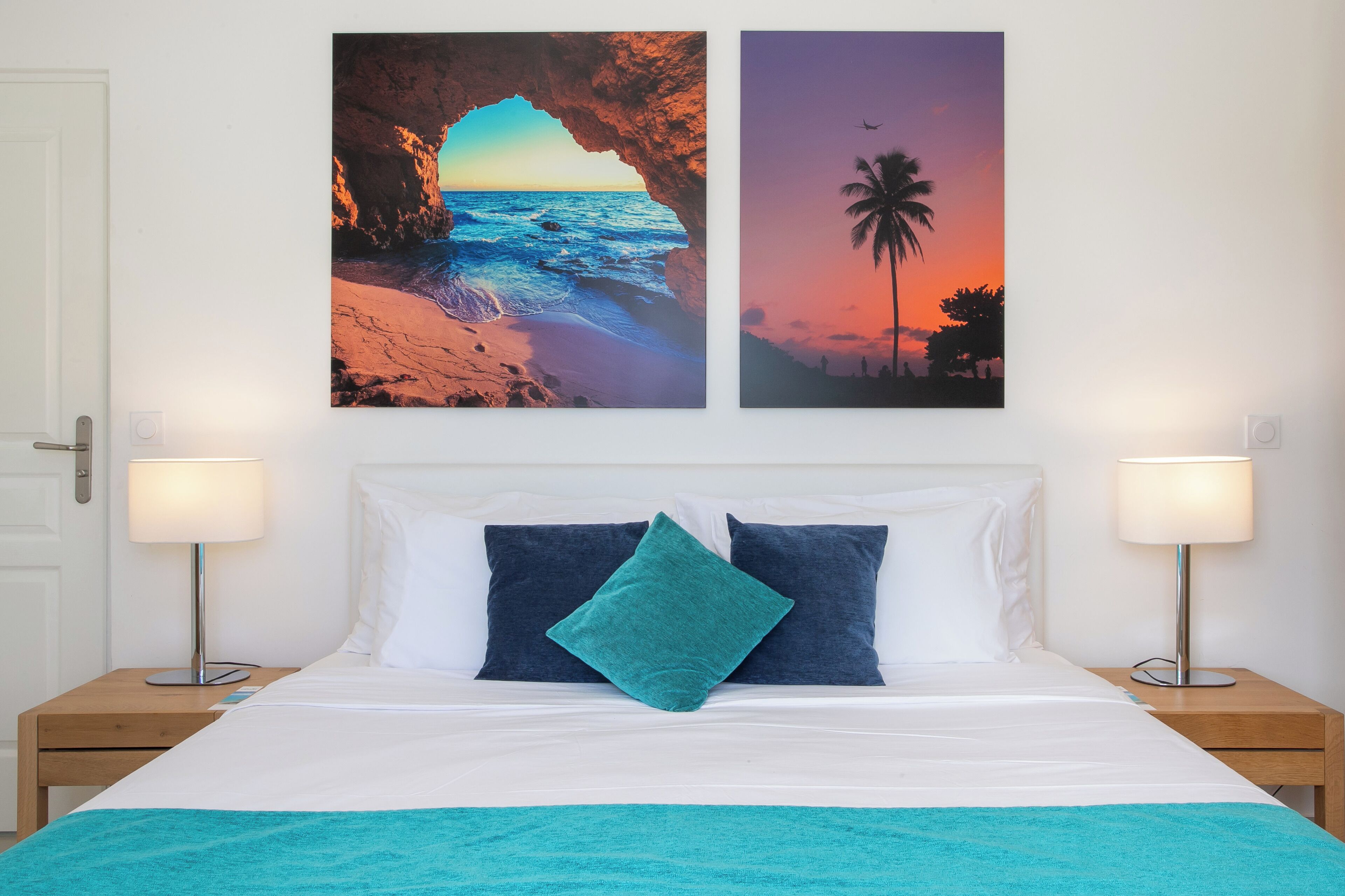 A hotel room with a bed, two nightstands, two wall-mounted lamps, and two framed pictures depicting a beach scene.