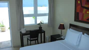 Habitación de hotel con cama, escritorio, silla, lámpara, teléfono y ventana con cortinas.