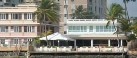 A beachfront hotel with multiple floors, palm trees, and a pool area.