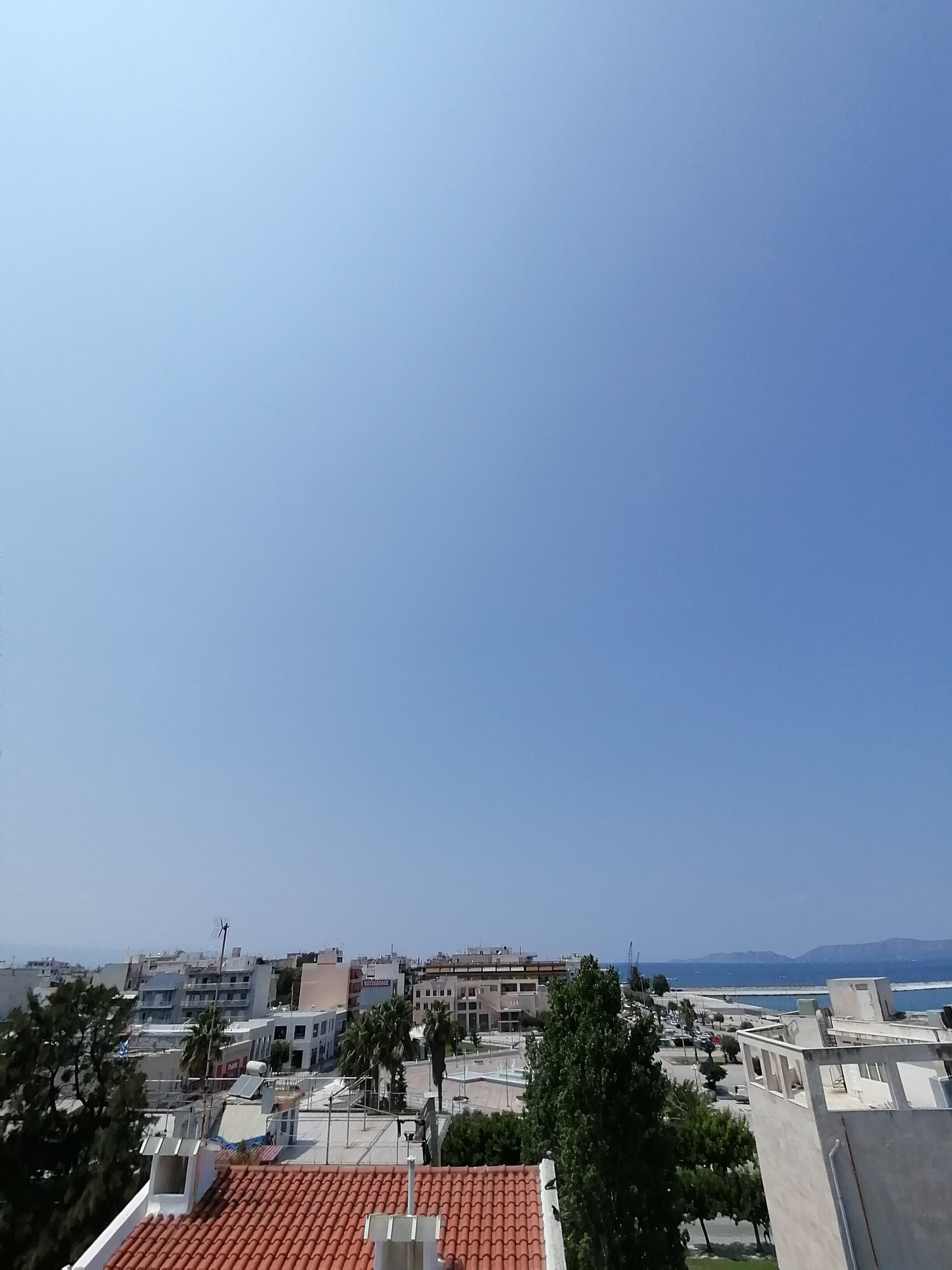 Paisatge urbà costaner amb edificis, alguns amb teules vermelles, i un cel serè.