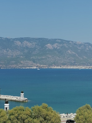 A coastal view with a lighthouse, rocky shoreline, and a distant cityscape.