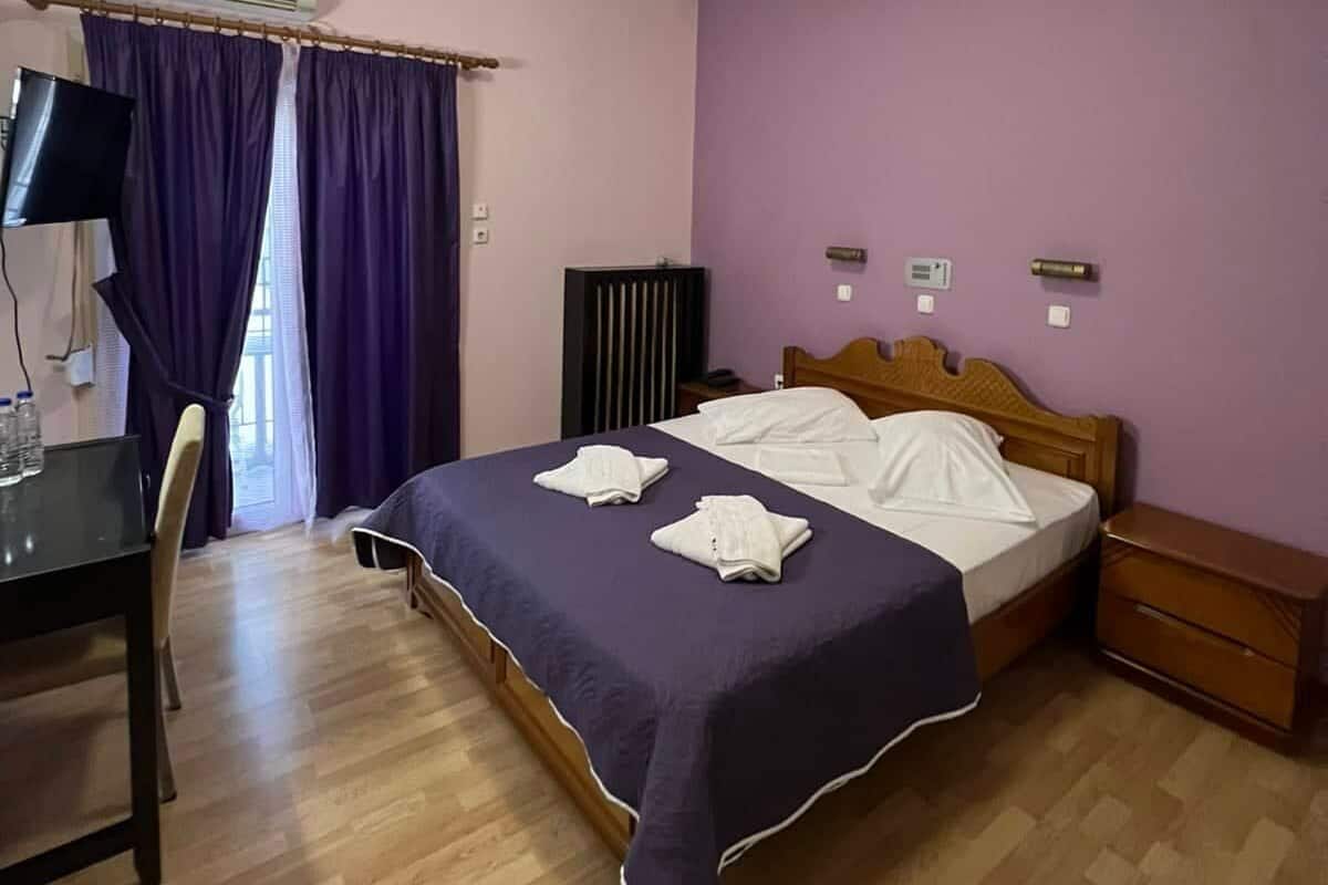 A room with a bed, a desk, a chair, an air conditioner, and a television.