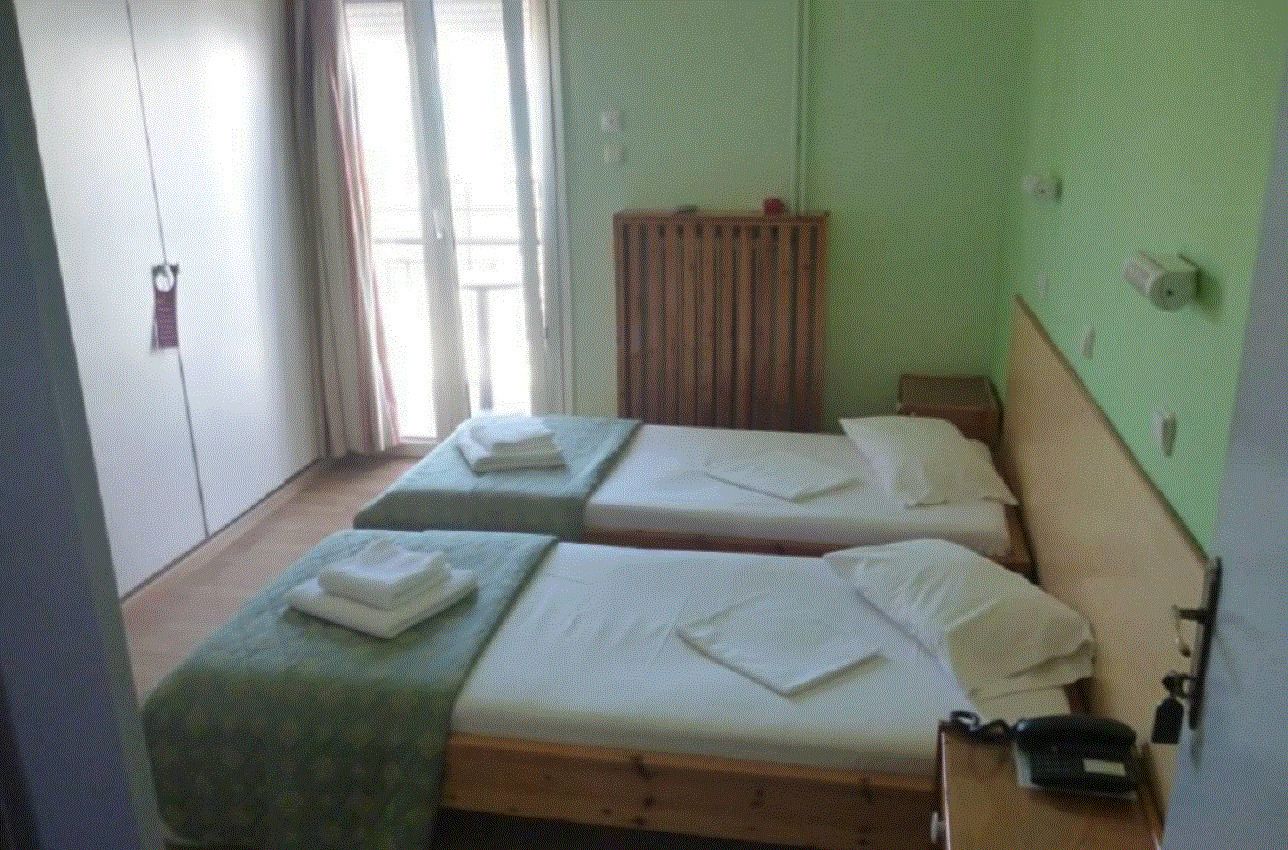 A room with two single beds, a wooden headboard, a small table with a telephone, and a window with curtains.