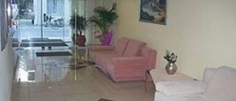 A hotel lobby with a reception desk, a pink sofa, a white sofa, and a patterned rug.