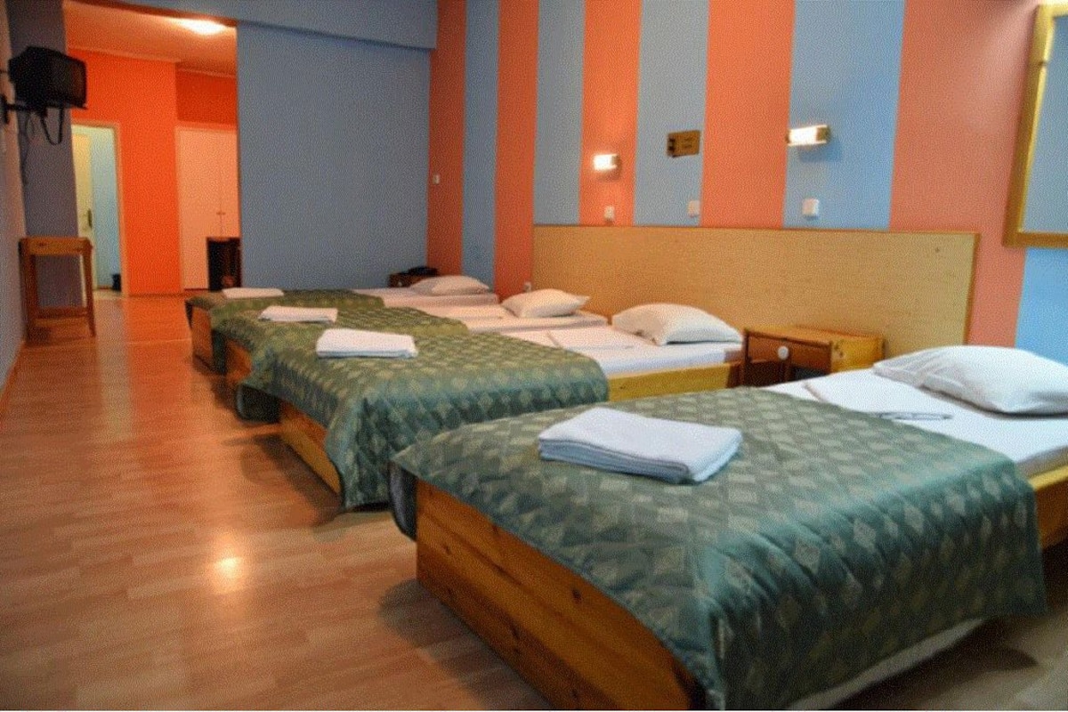 A hotel room with three beds, wooden headboards, and a tiled floor.