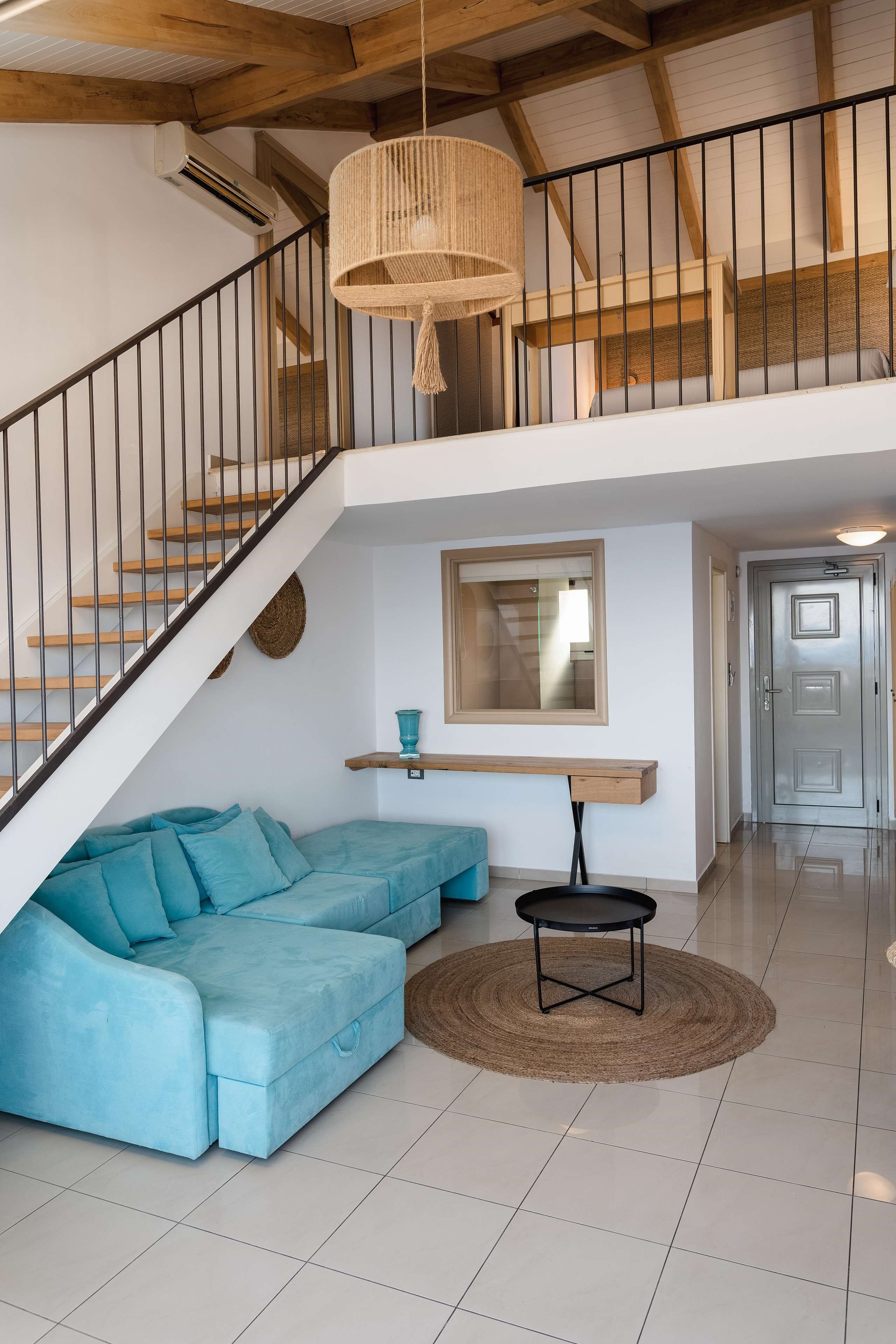 Amplia sala de estar con un sofá seccional azul, una mesa de centro redonda y una escalera con barandal negro.