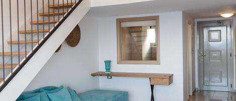 Amplia sala de estar con un sofá seccional azul, una mesa de centro redonda y una escalera con barandal negro.