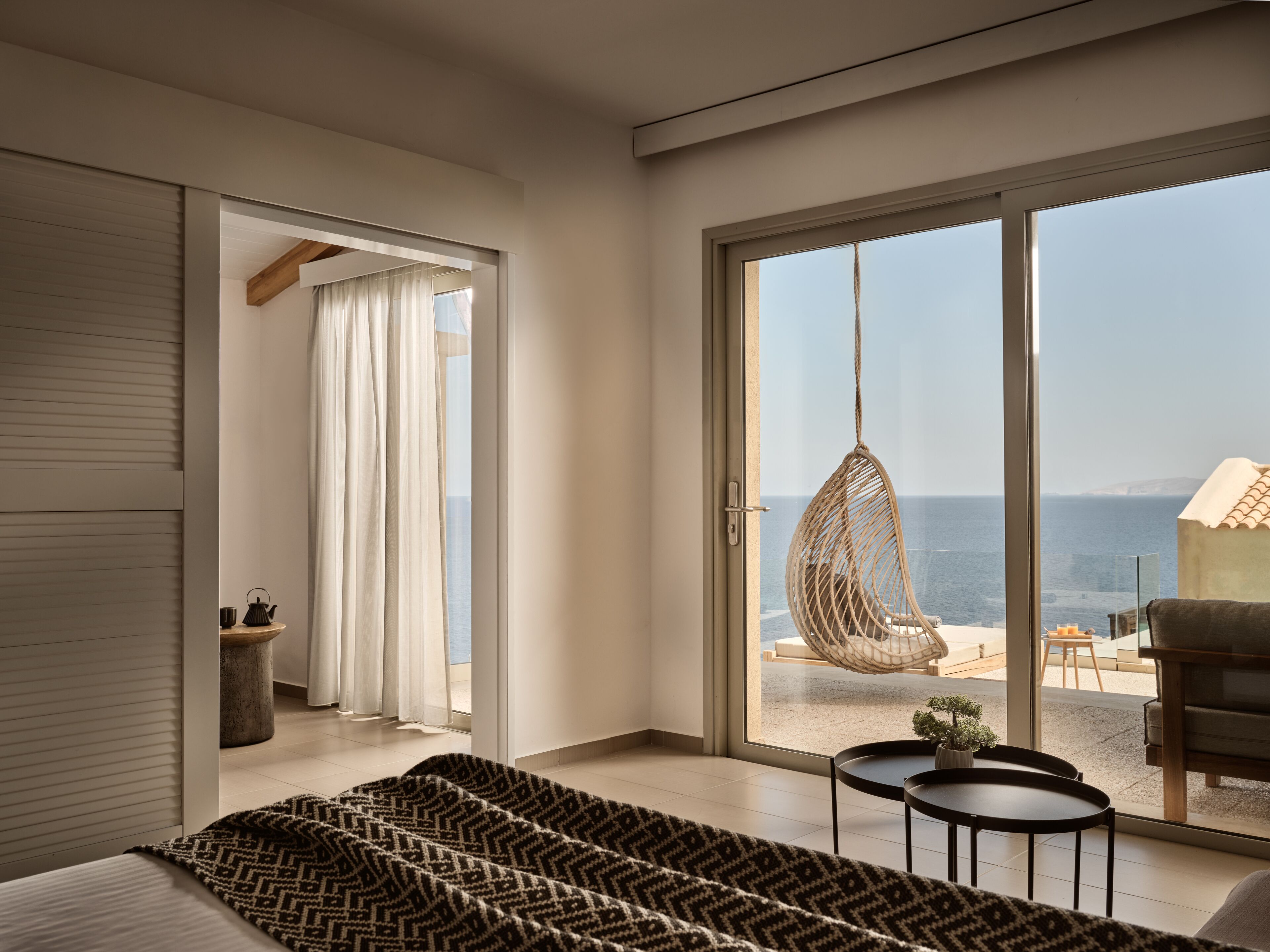 Ein modernes Hotelzimmer mit einer großen Schiebeglasdoor, die auf einen Balkon mit einer Hängematte und Meerblick führt.