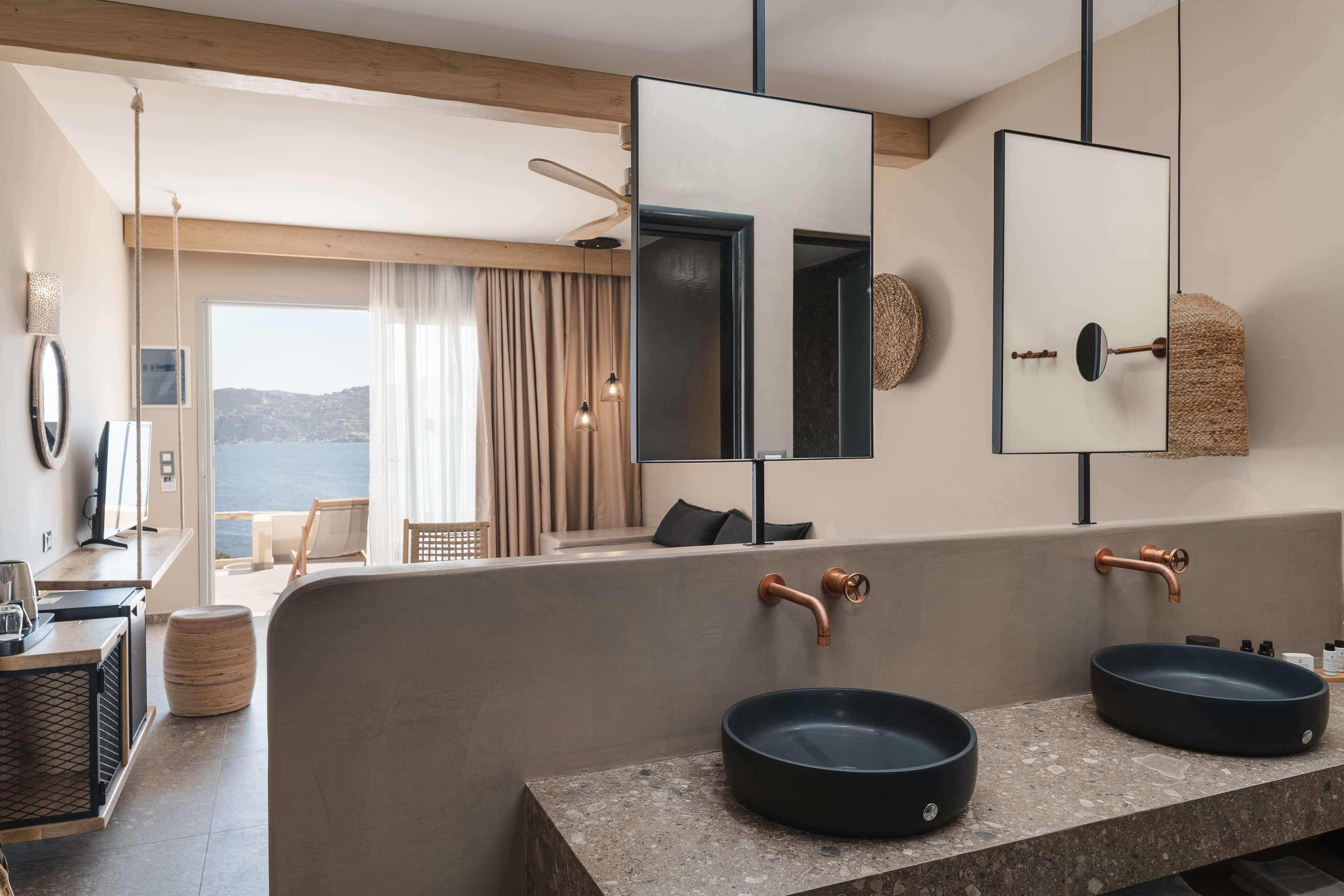 A modern bathroom with two black sinks, a large mirror, and a view of the sea.