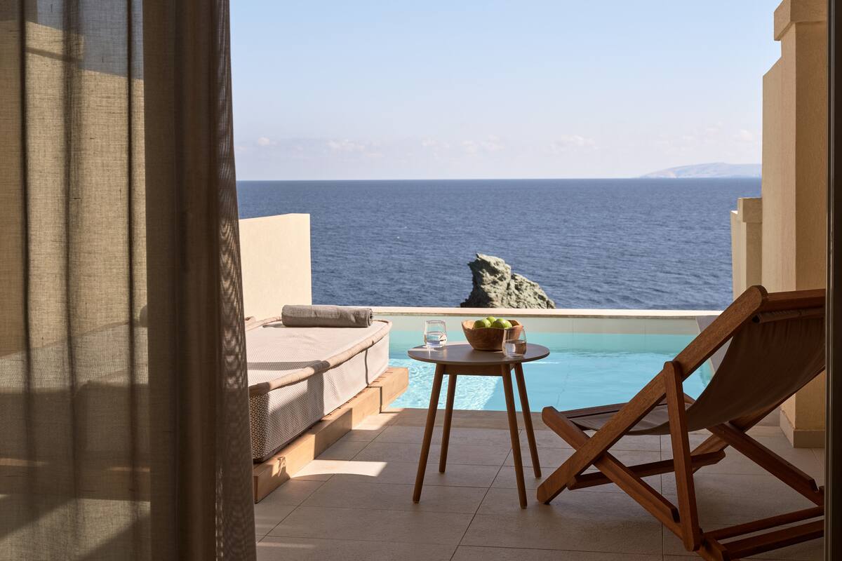 A balcony with a view of the sea, a pool, and a wooden chair.
