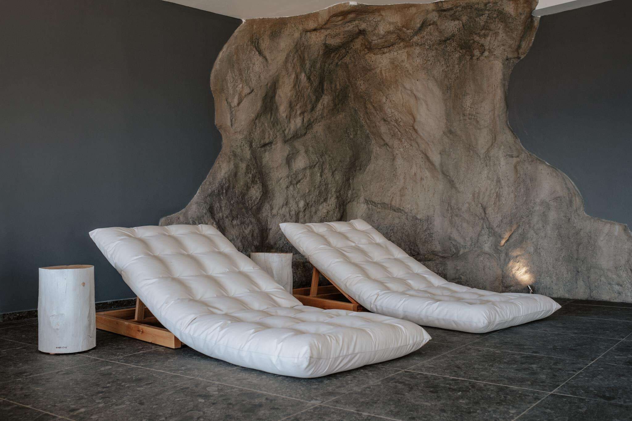 A room with two white cushioned benches against a large, textured wall.