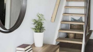 A staircase with wooden steps and a metal railing, a white wall, a round mirror, a potted plant, and a wooden shelf with books.
