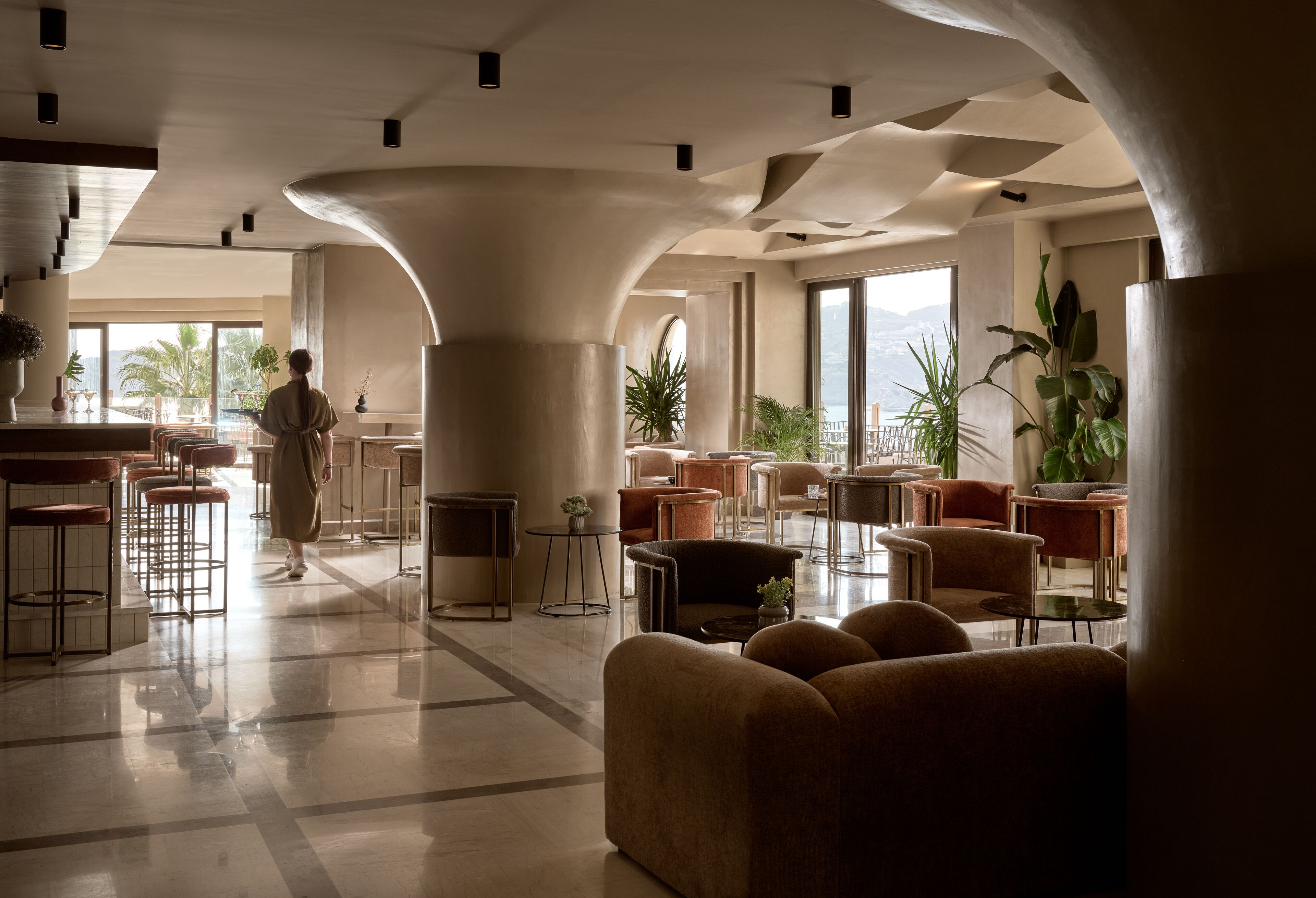 Un hall d’entrée spacieux, doté de hauts plafonds, de grandes fenêtres et d’un assortiment de coins salon comprenant des canapés et des tabourets de bar.