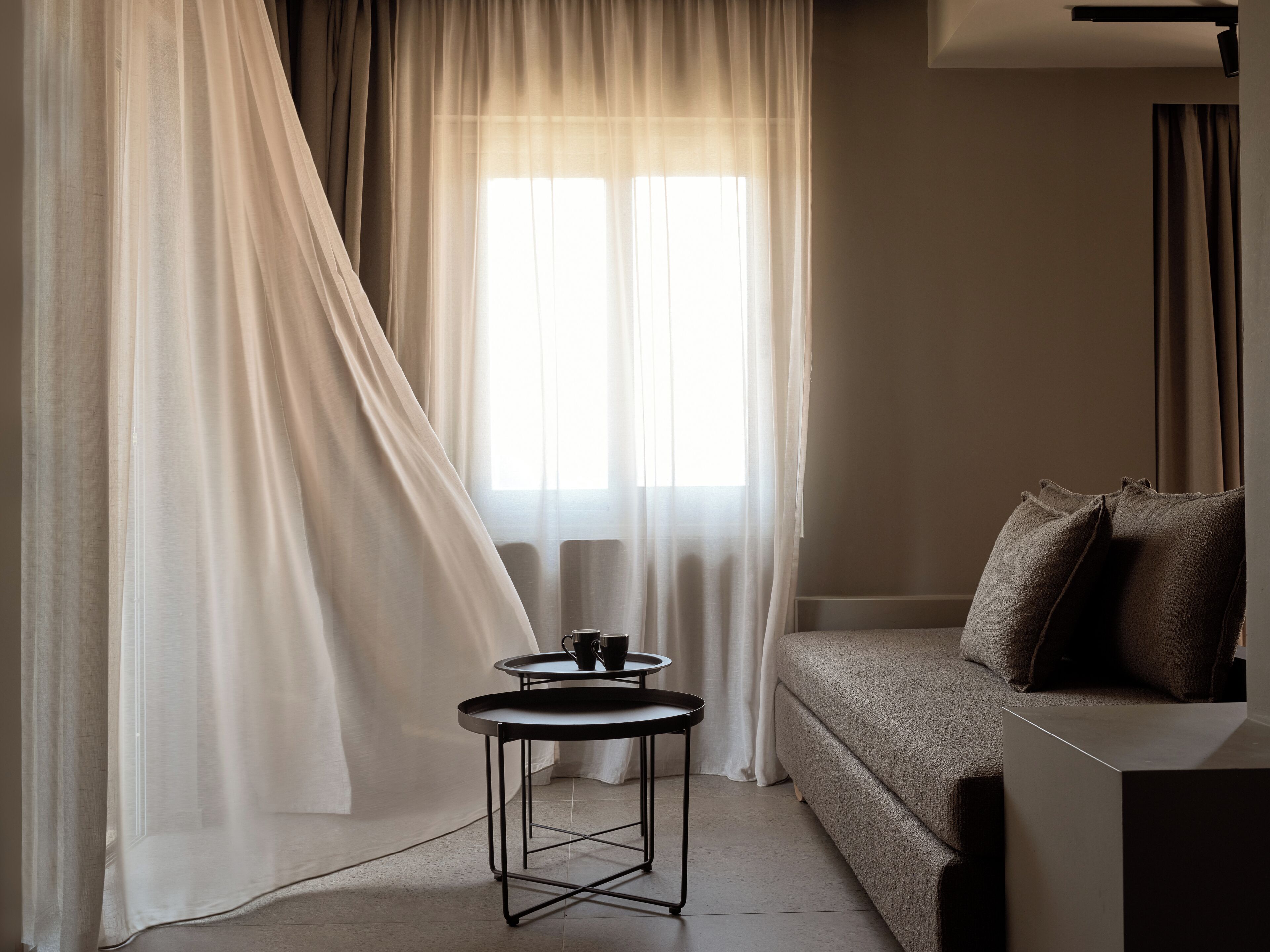 A room with a sofa, a small round table with a cup, and sheer curtains.