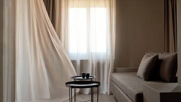 A room with a sofa, a small round table with a cup, and sheer curtains.