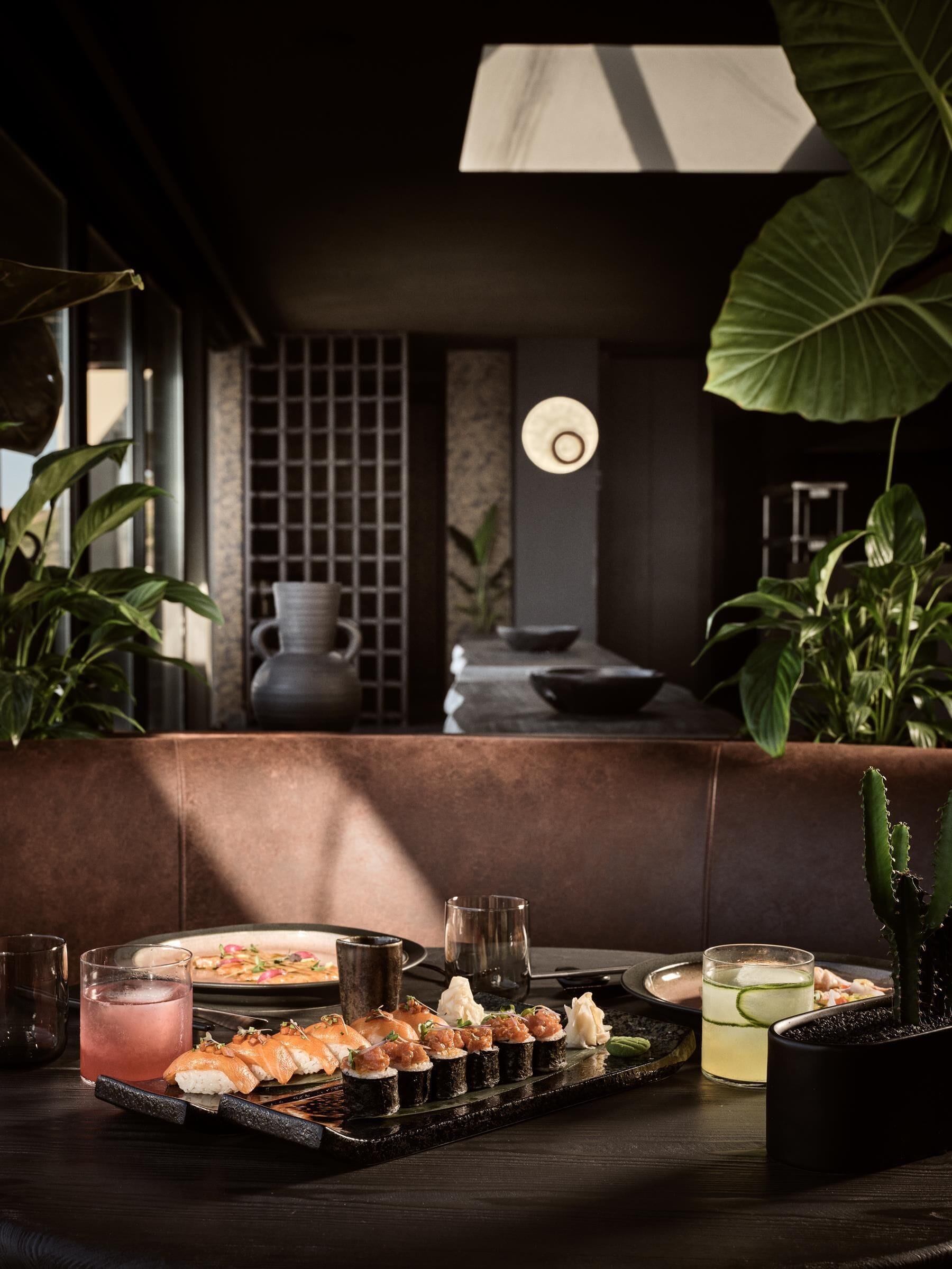 A dining area with a sushi platter, drinks, and a large plant.