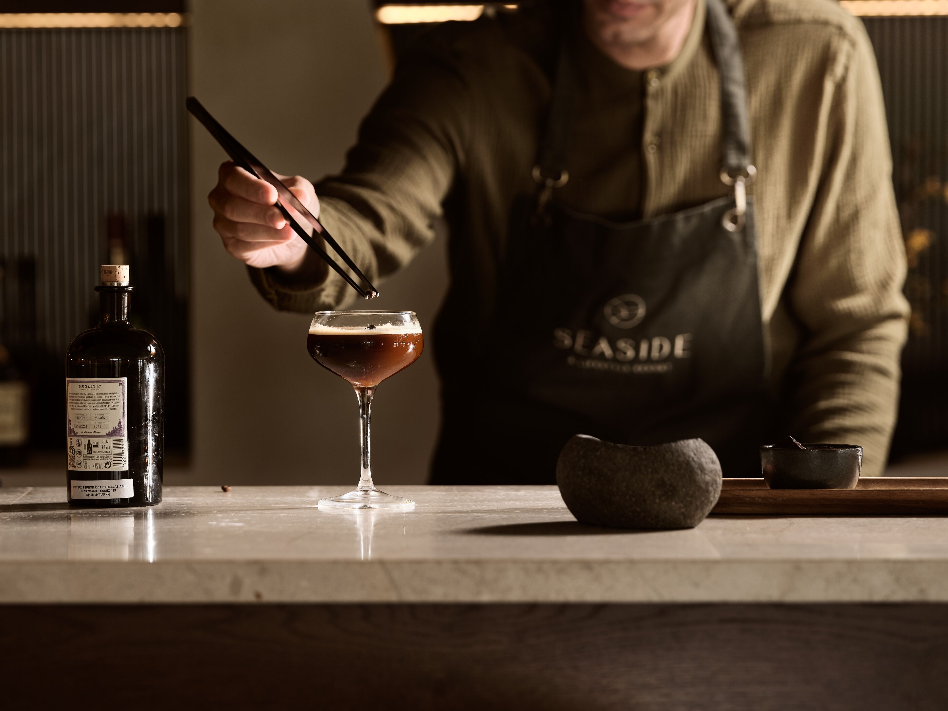 Ein Barkeeper bereitet ein Getränk mit einer Flasche mit dem Aufdruck "MONKEY 47" und einem Glas auf der Theke zu.