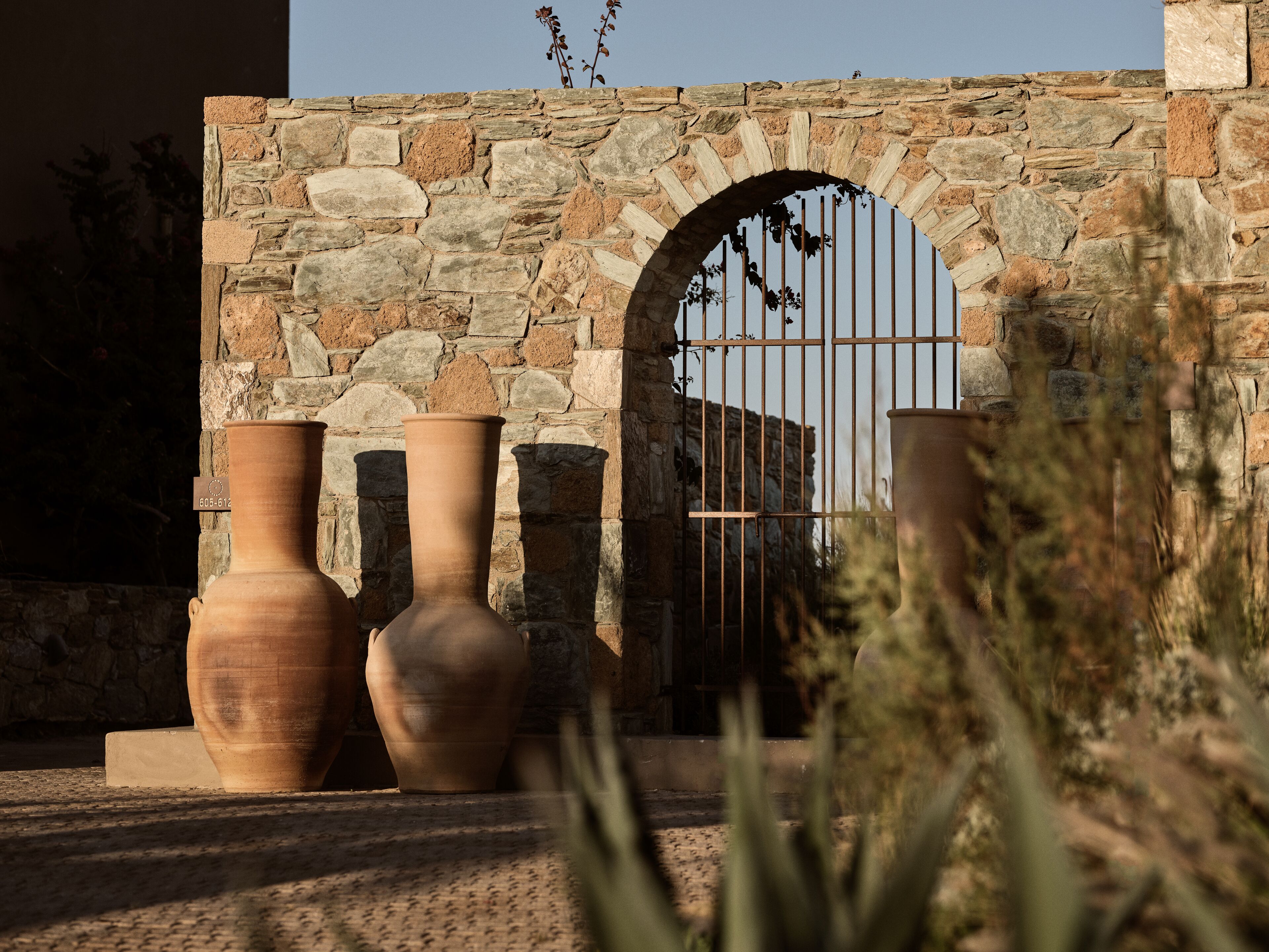 A stone wall with an arched entrance and three large terracotta pots in front.