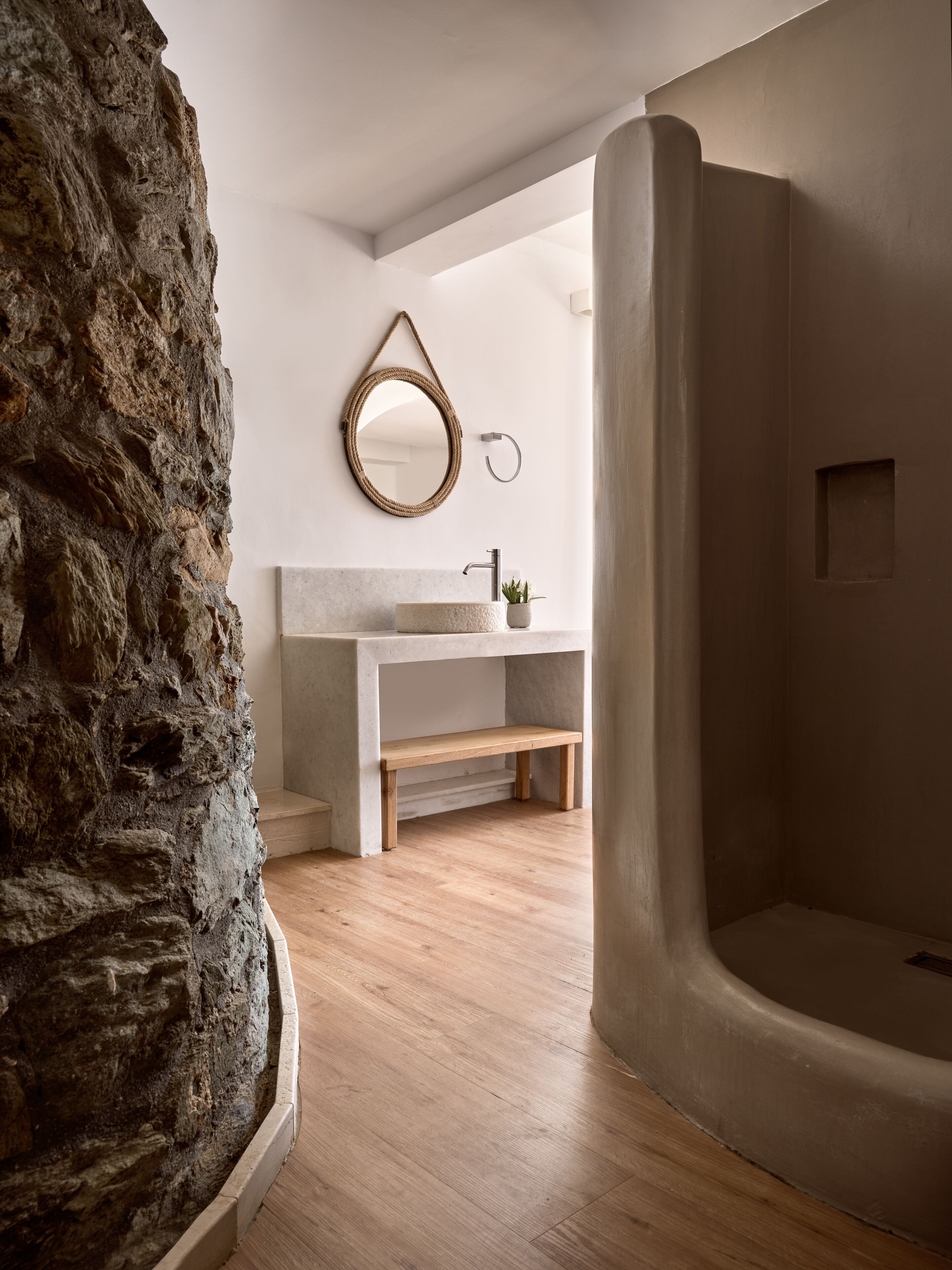 A bathroom with a stone wall, a round mirror, a sink, and a bathtub.