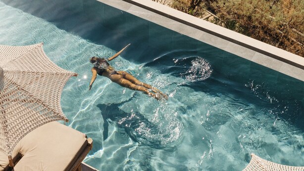 A swimming pool with clear water, a person swimming, and a view of the sea. - Seaside A Lifestyle Resort All Inclusive (Malevizi)