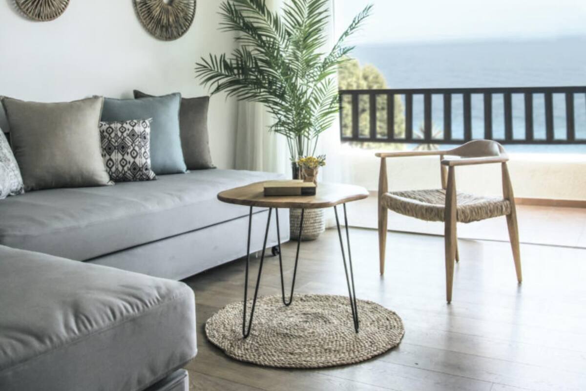 A modern living room with a sofa, a round table, a chair, a hanging light fixture, and a view of the ocean.