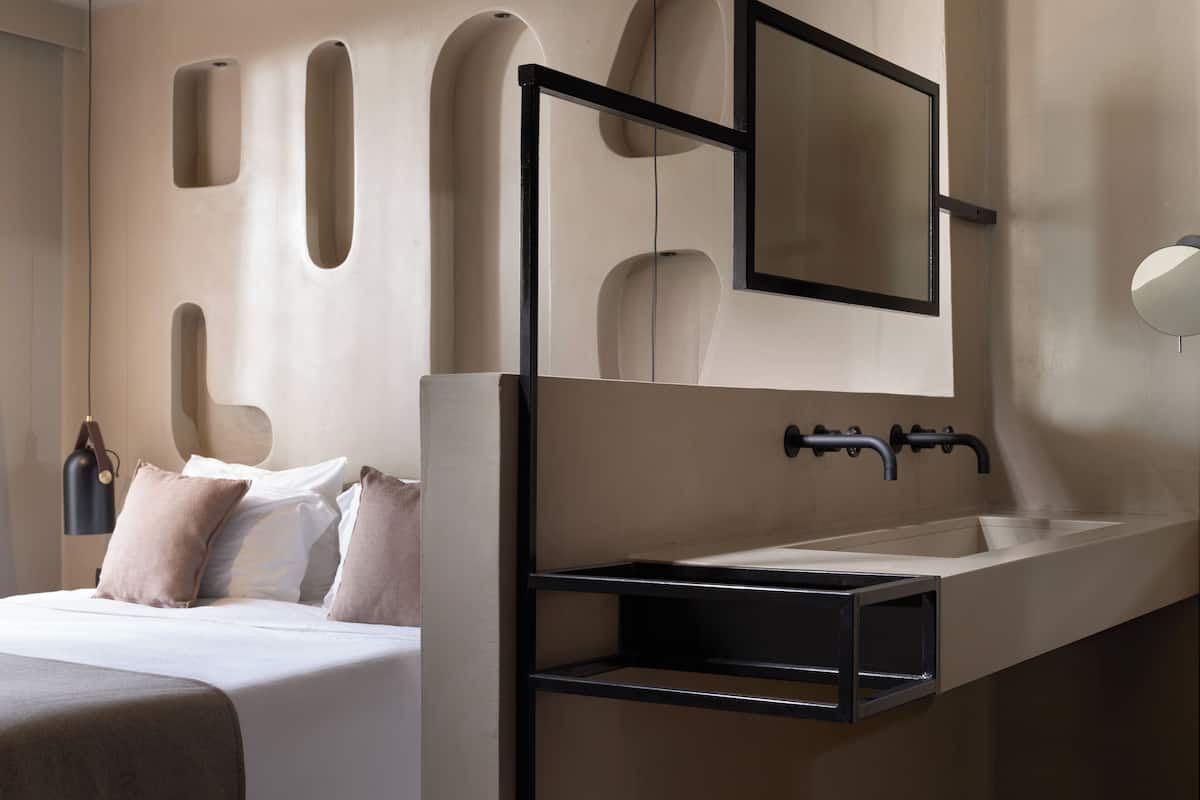 A modern hotel room with a bed, a built-in sink, and a mirror above it.