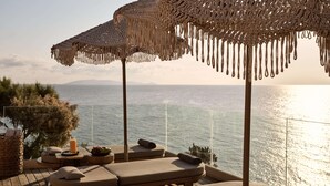 A sunlit outdoor lounge area with cushioned seating and a view of the sea. - Seaside A Lifestyle Resort All Inclusive (Malevizi)
