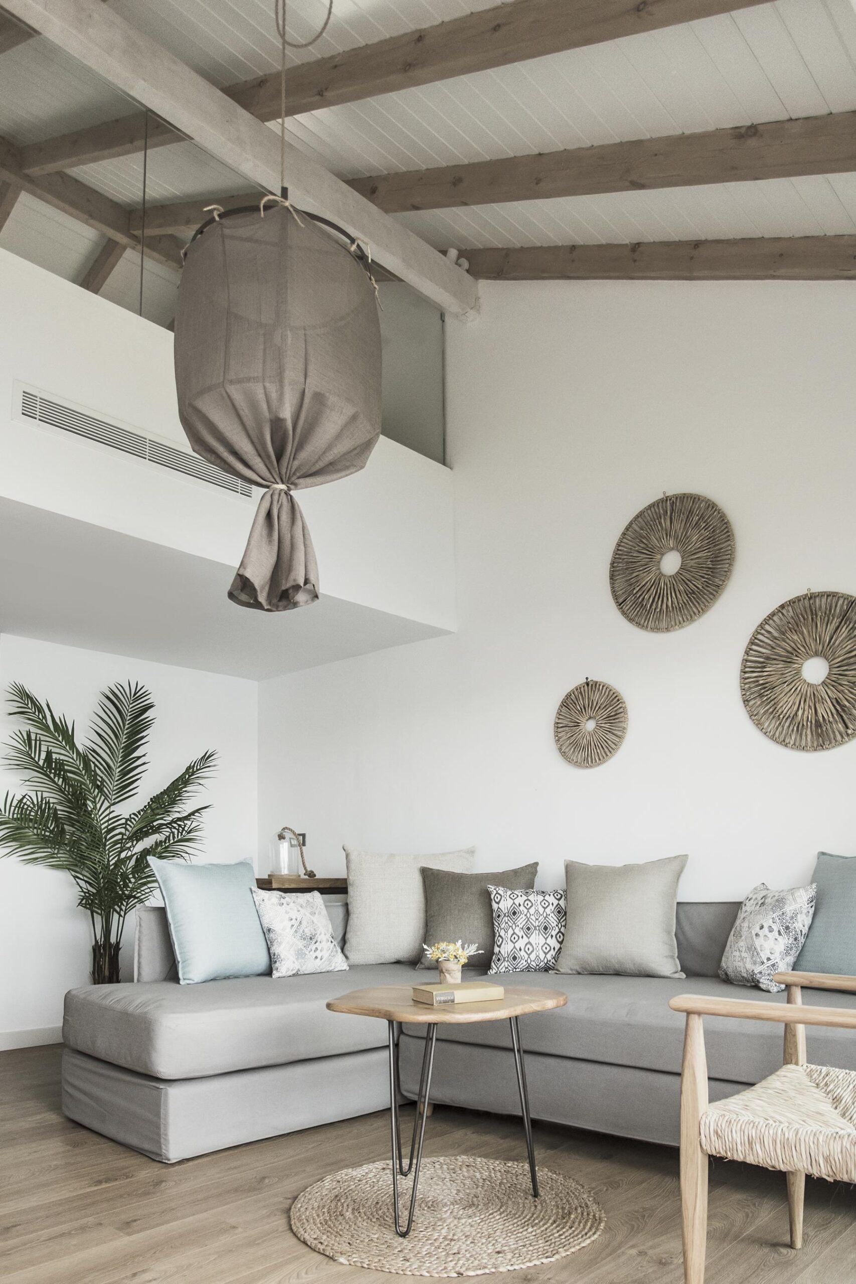 Un salon moderne avec un canapé gris, une table basse ronde et un luminaire suspendu.