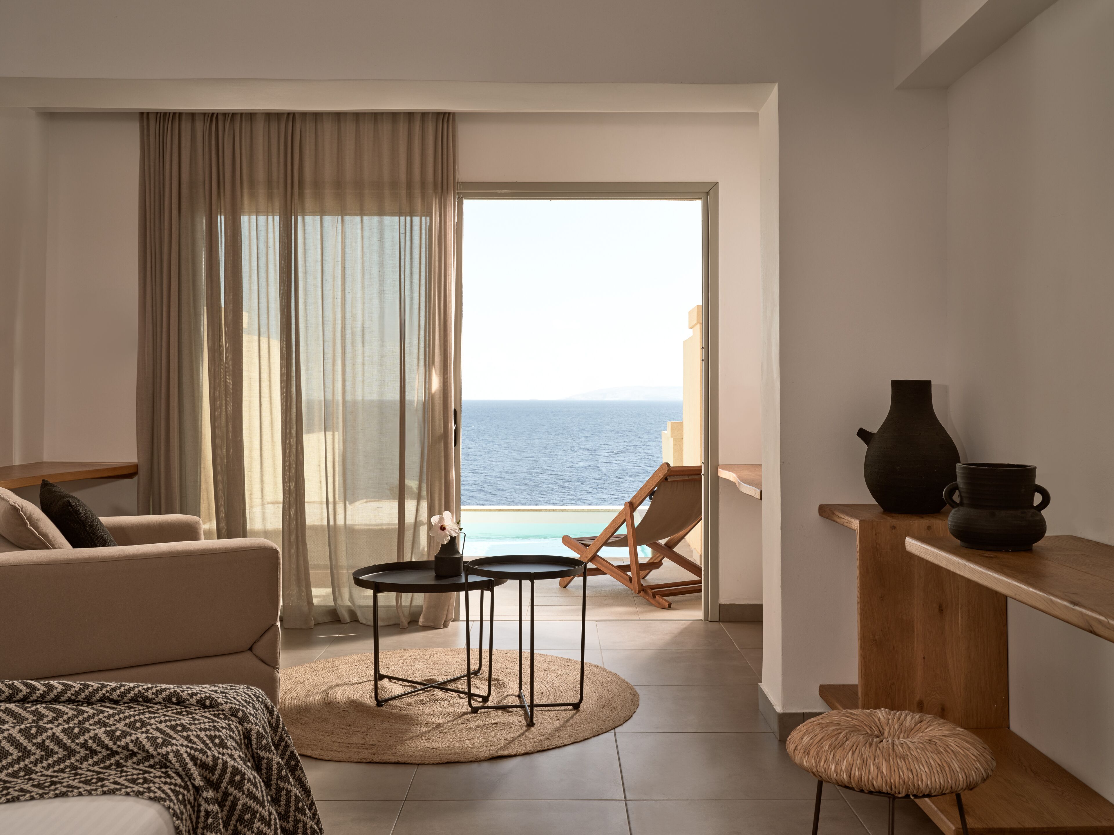 A modern living room with a view of the sea, a balcony, and a small table with a vase.