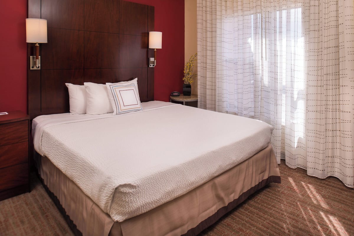 A large bed with a wooden headboard, two bedside lamps, and a vase with flowers on a nightstand.