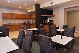 Habitación de hotel con kitchenette, zona de comedor con mesas y sillas, y televisor de pantalla plana montado en la pared.