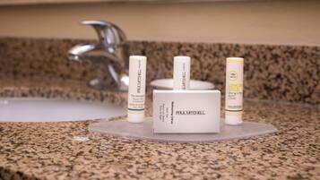 Una encimera de baño con cubierta de granito, un grifo plateado y tres botellas de artículos de aseo con las etiquetas "Paul Mitchell" y "Lemon Sage".